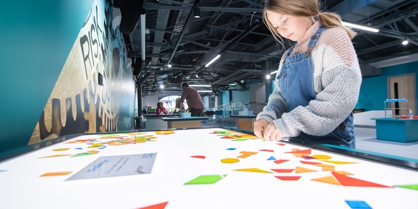 A photograph of a girl at Aberdeen Science Centre. The girl is playing with shapes on a light table.