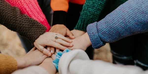 Eight hands reaching in to a circle of people and touching in the middle.