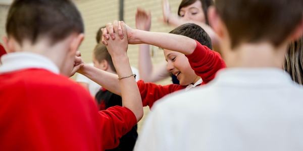 A close up of school children, wearing red and white uniforms, holding hands during ceilidh dancing.