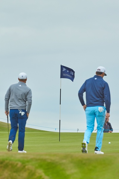Two golfers on a golf course, with a flag on a flagpole in between them.
